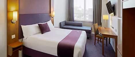 A hotel room with a large bed, a small sofa, a desk, and a TV.