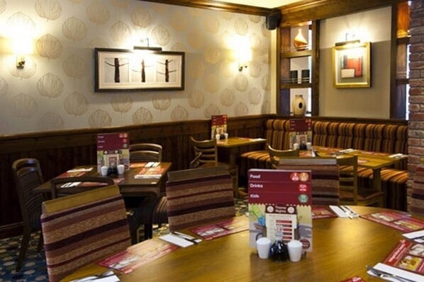 A restaurant with wooden tables and cushioned booths, menu stands, and framed artwork on the walls. - Premier Inn Wirral (Ellesmere Port)