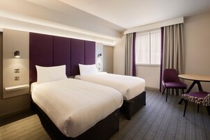 A hotel room with two beds, a desk, and a chair.