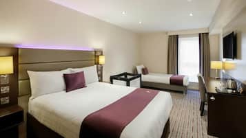 A hotel room with a large bed, a smaller bed, a desk with a chair, a TV, and a window with curtains.