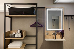 Habitación de hotel compacta con literas, un pequeño estante de madera con artículos de tocador, un espejo con marco de madera y un secador de pelo en un estante.