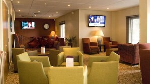 Een hotellobby met verschillende zithoeken, een aan de muur bevestigde televisie en een klok.
