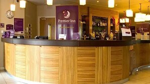 Zona de recepción de Premier Inn con un mostrador de madera, un reloj y un letrero sobre el mostrador.