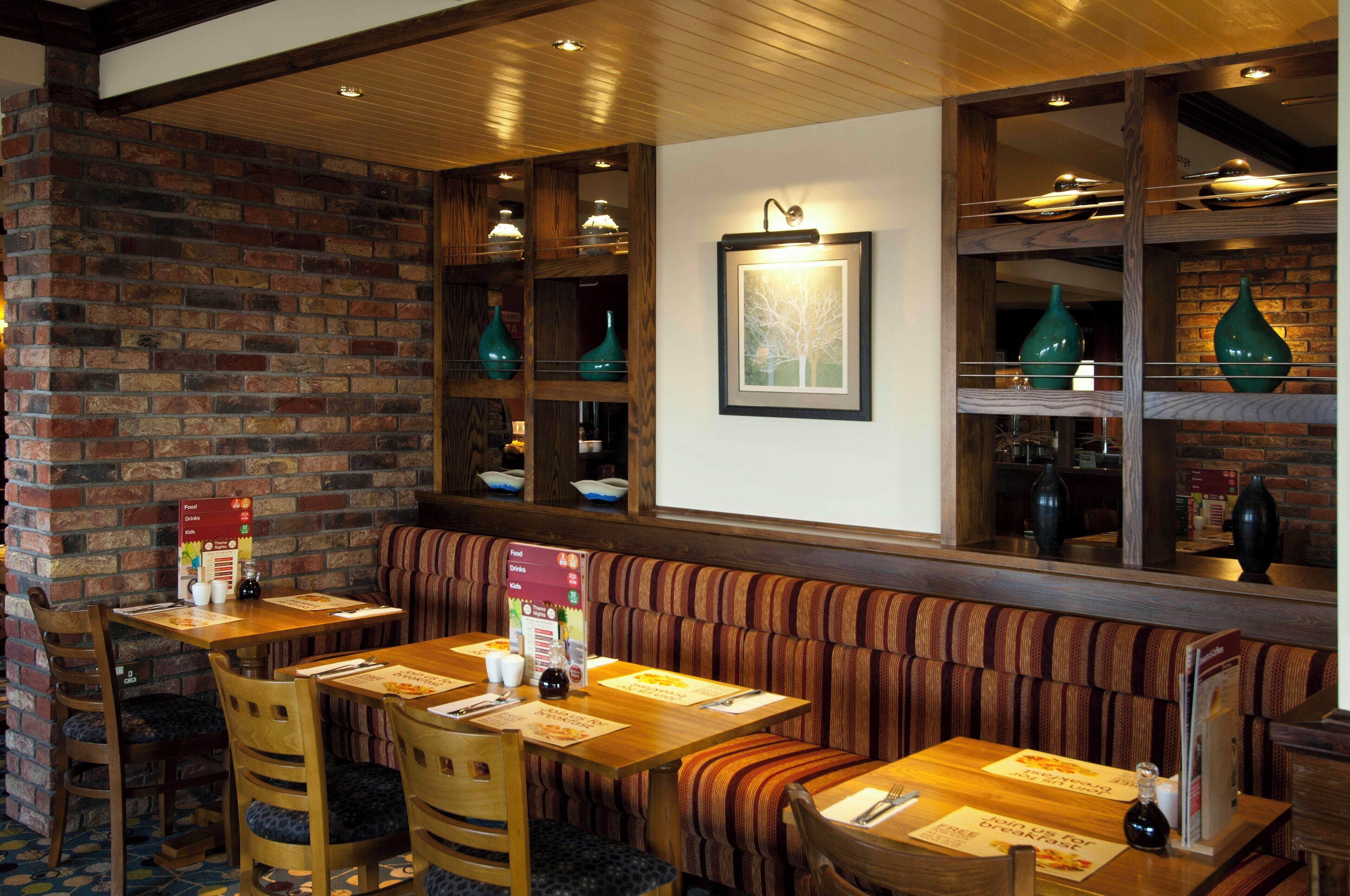 A restaurant with brick walls, wooden tables, striped booths, and hanging light fixtures.
