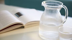 Une carafe en verre transparent et un verre sont posés sur une table, à côté d’un livre ouvert.