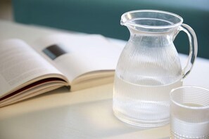 Ein durchsichtiger Krug und ein Glas neben einem offenen Buch auf einem Tisch.