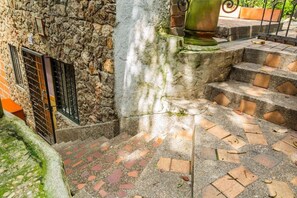 Mur de pedra amb una reixa metàl·lica, una escala de pedra i una gran jardiniera verda.