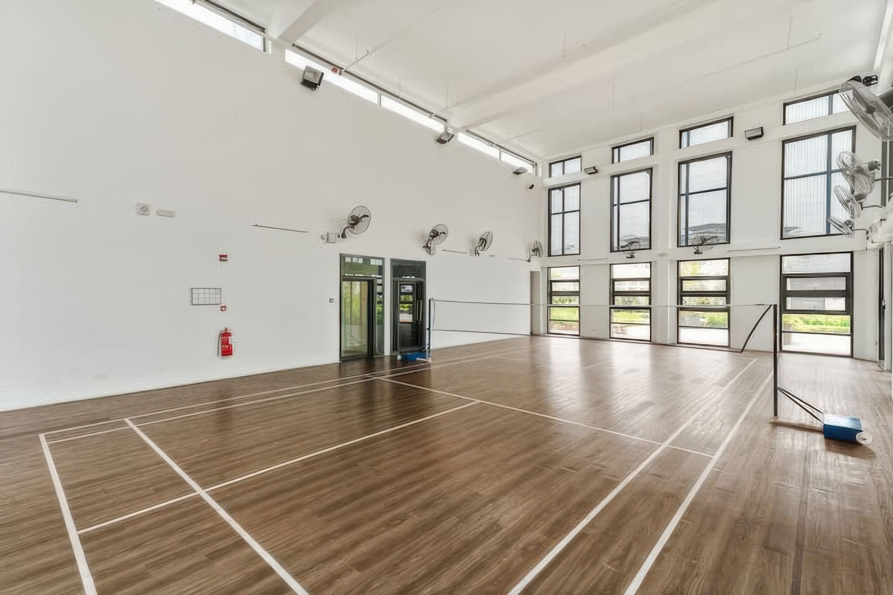 Ein großzügiger Innenbereich mit Holzboden, großen Fenstern und Deckenventilatoren.