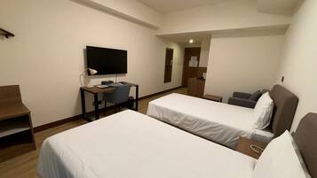 A hotel room with two single beds, a desk with a chair, a television, and a small table.