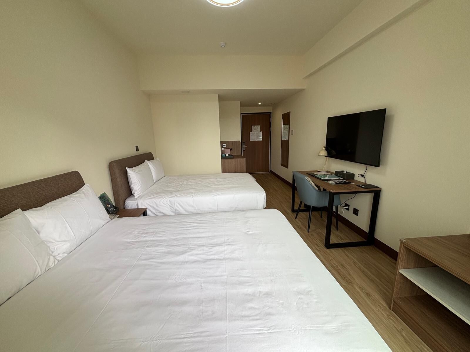 Een hotelkamer met twee enkele bedden, een bureau met stoel, een flatscreen televisie en een deur naar een gang.