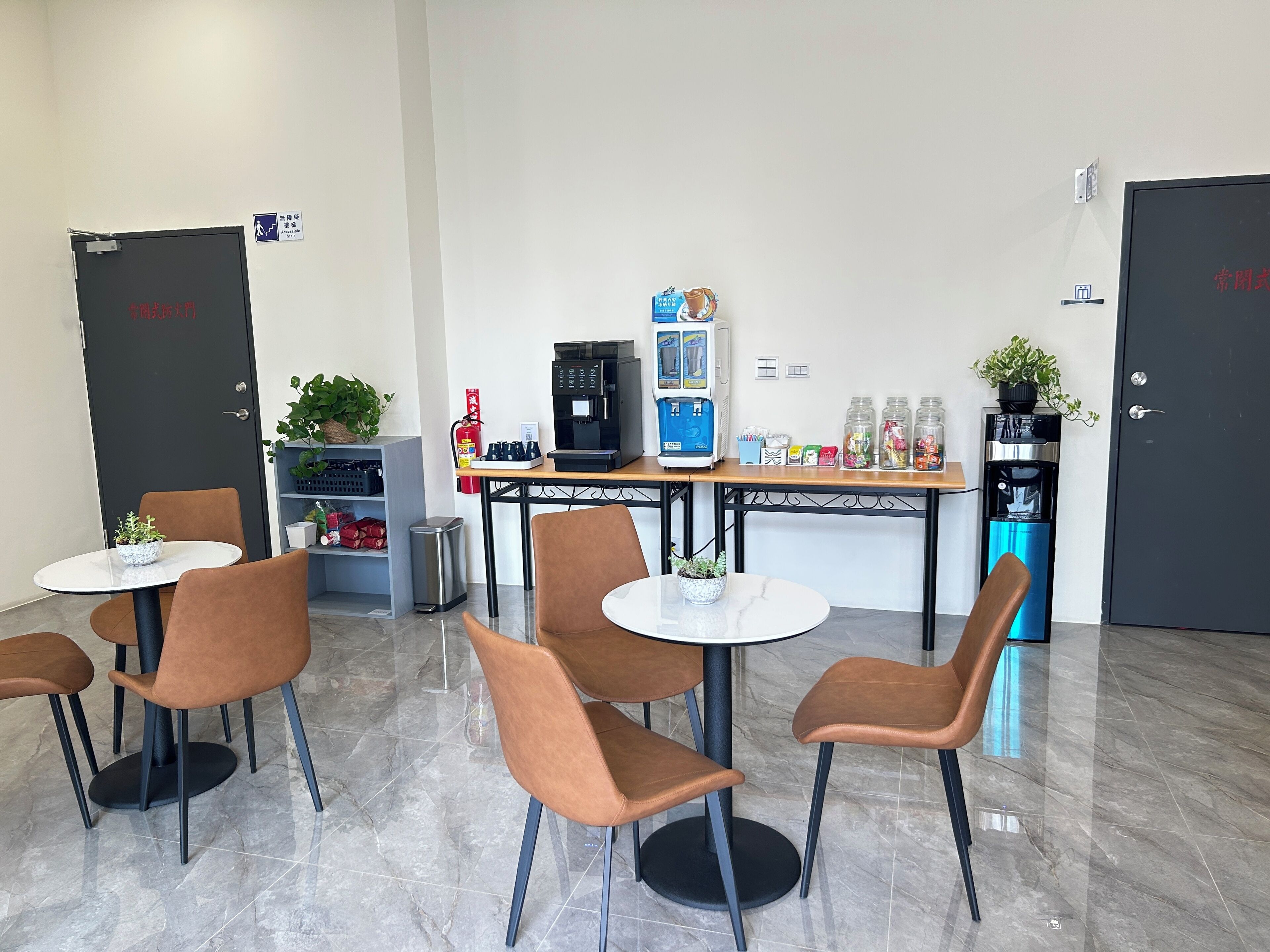 Un espai d'oficina modern amb una màquina de cafè, un dispensador d'aigua i una planta petita sobre una taula.