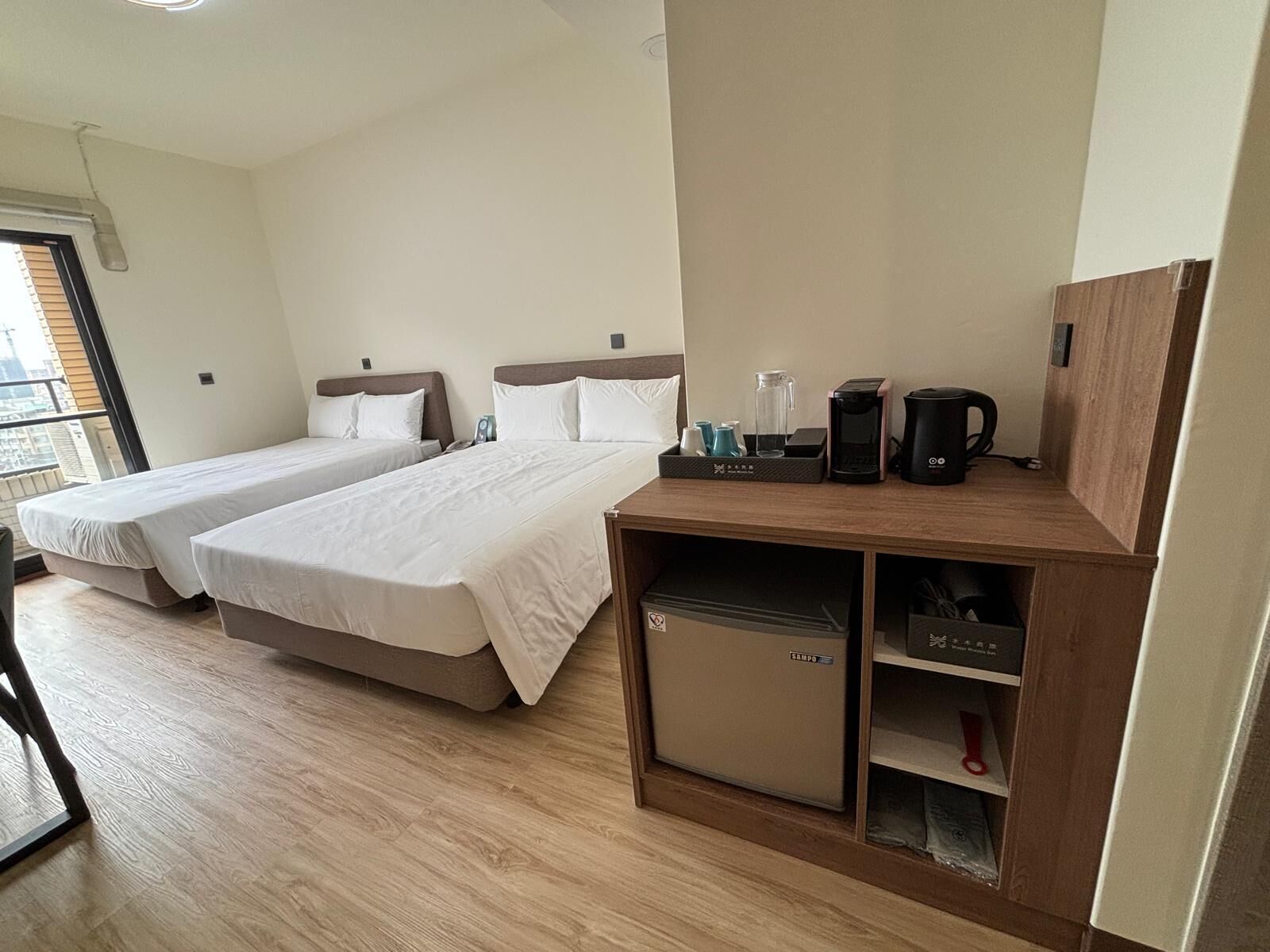 A hotel room with two beds, a small kitchenette, and a view of the city.
