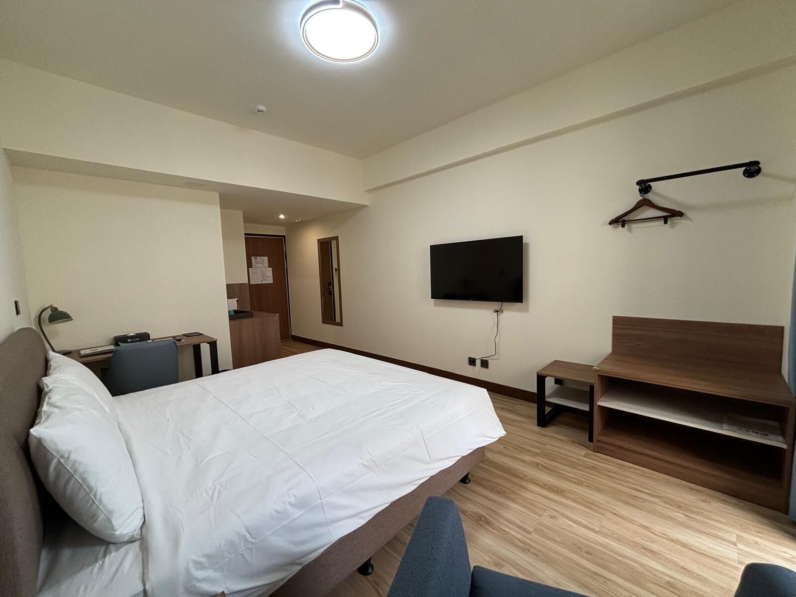 Une chambre d’hôtel comprenant un lit, un bureau, une chaise, un téléviseur fixé au mur et un banc en bois.