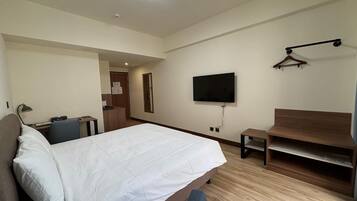 Une chambre d’hôtel comprenant un lit, un bureau, une chaise, un téléviseur fixé au mur et un banc en bois.