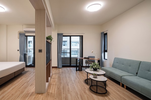 Una sala moderna con un sofá, una mesita con una planta, un escritorio con una silla y una cama.