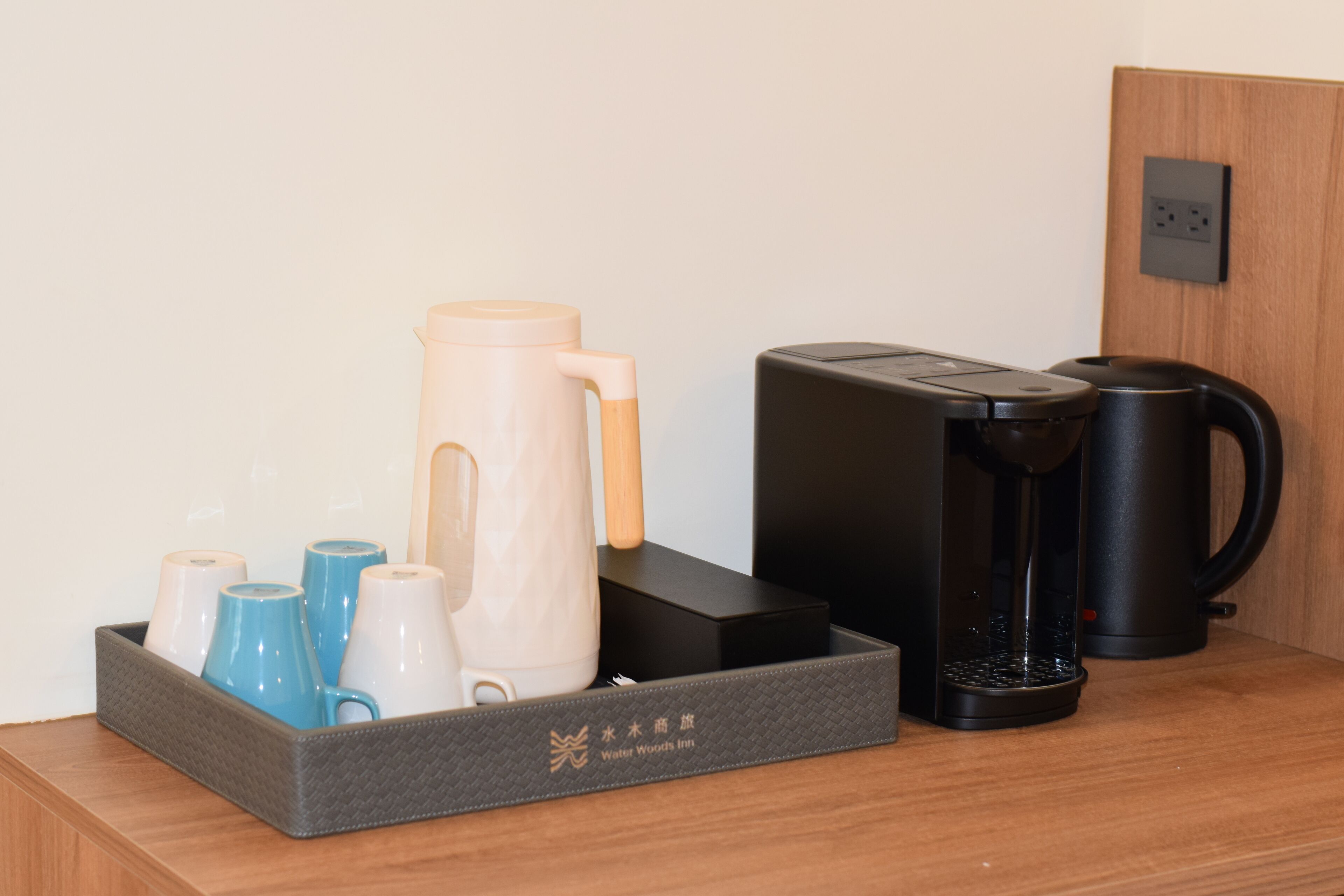 Une machine à café, un pichet d’eau et un plateau avec des tasses, le tout posé sur une table en bois.
