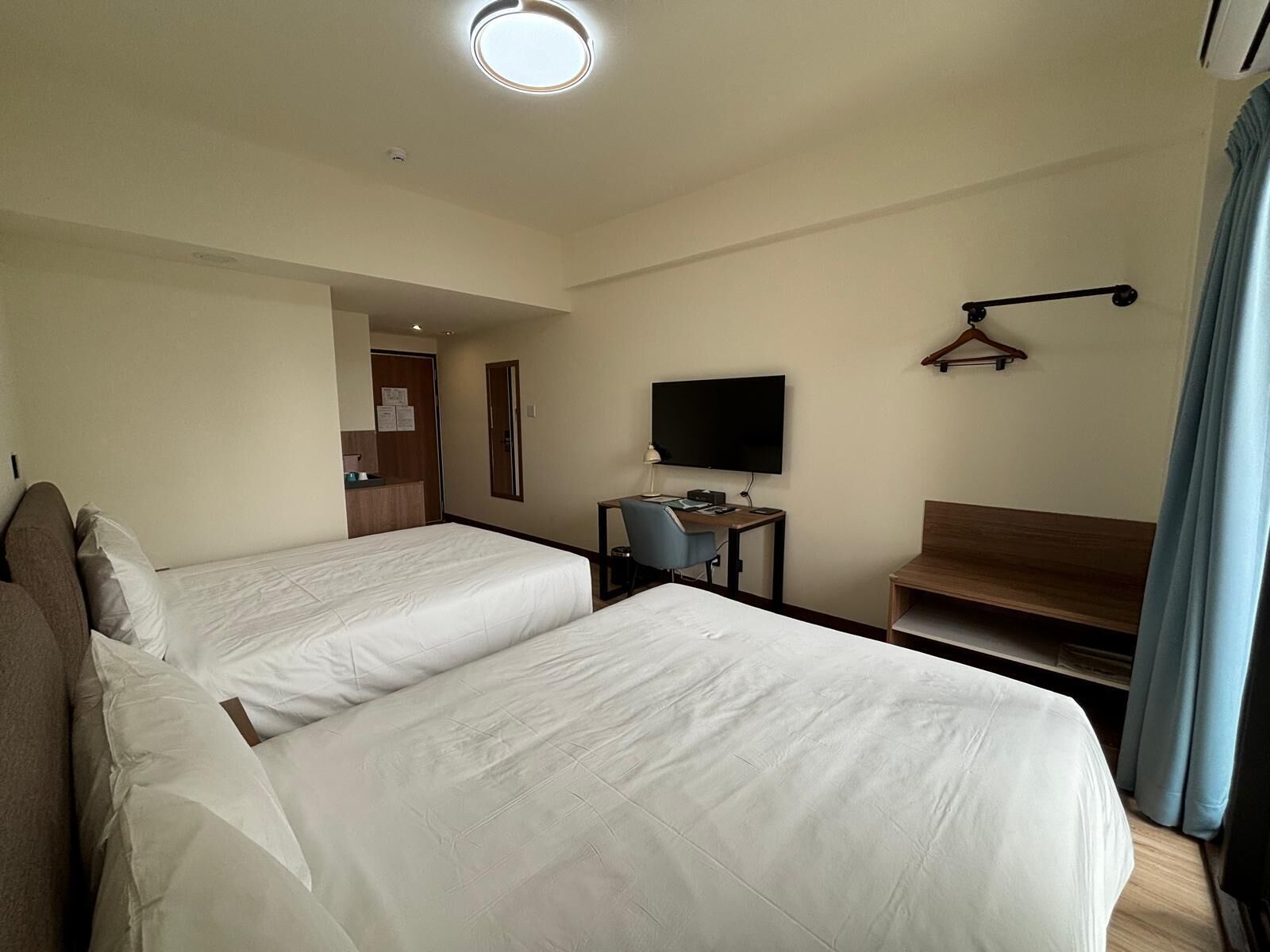 A hotel room with two beds, a desk with a chair, a TV, and a coat rack.