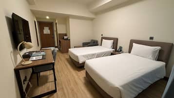 A hotel room with two single beds, a desk with a lamp, a chair, and a small table.