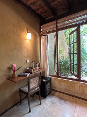 Une pièce comprenant un bureau en bois, une chaise, une petite table avec un vase de fleurs, une machine à café et une fenêtre avec des rideaux.