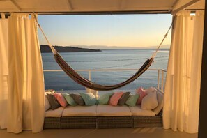 A hammock suspended over a cushioned seating area with a view of a calm sea and distant land. - Dream on The Beach - Panoramic Seaview Terrace (Kraljevica)