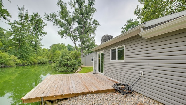 A house with a wooden deck extending over a body of water, surrounded by trees.