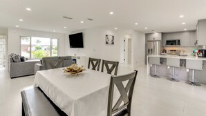 A modern kitchen with stainless steel appliances, a dining area with a white table and grey chairs, and a living area with a grey sofa and a flat-screen TV. - Swim, Golf & Explore: Pet-Friendly Cape Coral Home (Cape Coral)