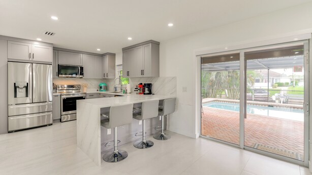 A modern kitchen with stainless steel appliances, a marble island, and a sliding glass door leading to a pool area. - Swim, Golf & Explore: Pet-Friendly Cape Coral Home (Cape Coral)