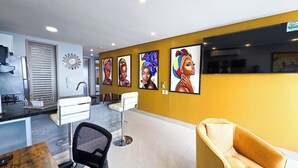 A modern kitchen with a built-in oven, a sink, and a refrigerator. There are two white bar stools and a yellow armchair.