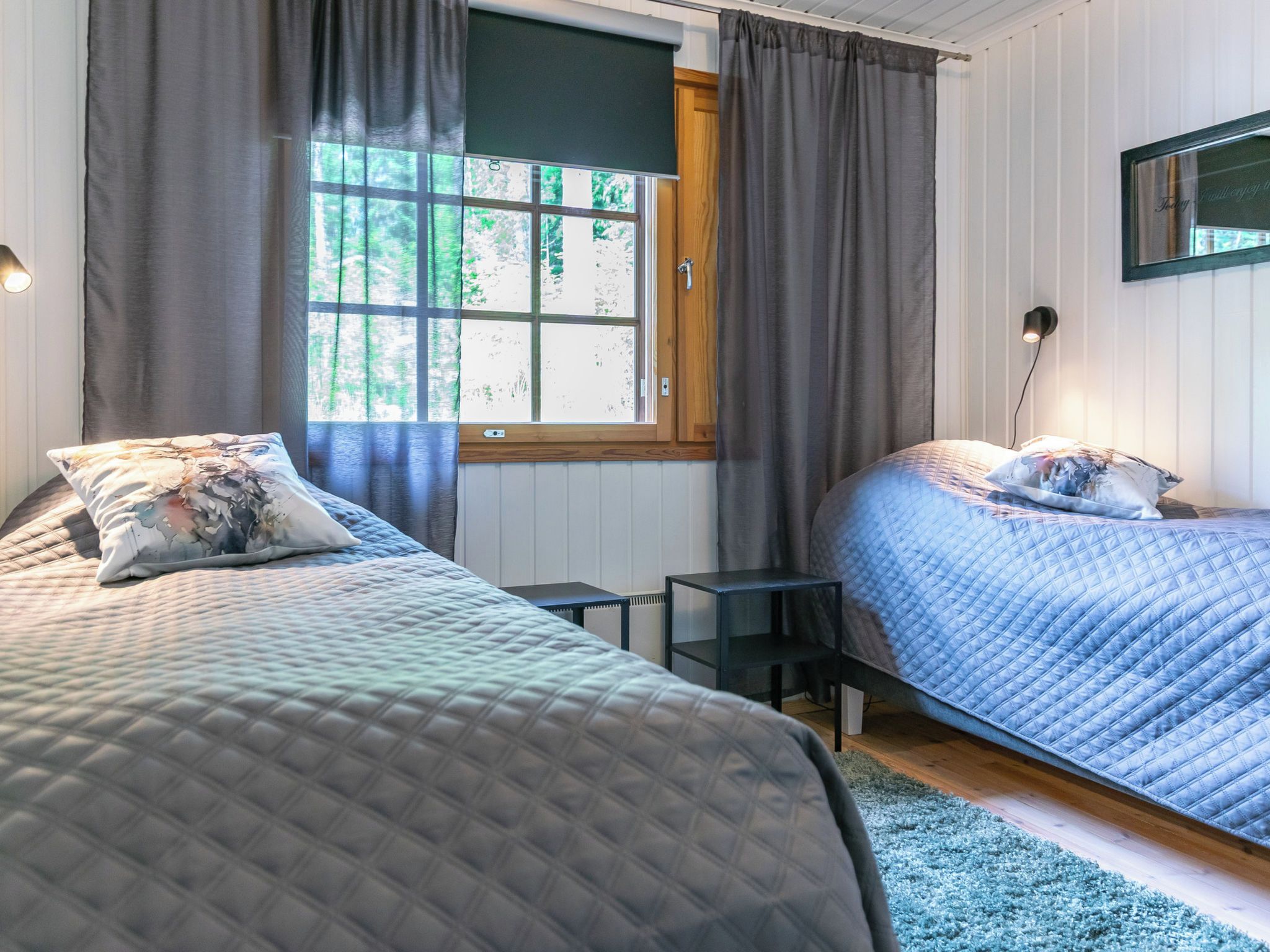 Ein Schlafzimmer mit zwei Betten, einem Fenster mit Vorhängen, einem Nachttisch und einer Wandlampe.