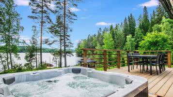 A hot tub on a wooden deck with a view of a lake and forest.