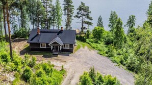 A two-story house with a dark roof and white trim, surrounded by dense forest and a lake. - Hanhenpesä by Interhome (Rautalampi)