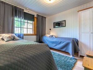 A bedroom with two beds, a window with curtains, a mirror, and a wooden door. - Hanhenpesä by Interhome (Rautalampi)