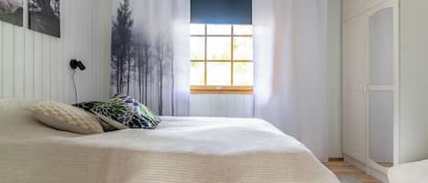 A bedroom with a large bed, a window with curtains, a wall-mounted lamp, and a wardrobe.