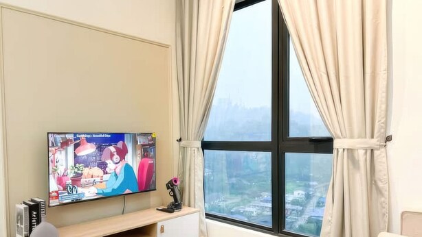 Un salon avec un téléviseur posé sur un meuble en bois, une table ronde et une vue sur le paysage urbain, visible à travers une grande fenêtre ornée de rideaux.