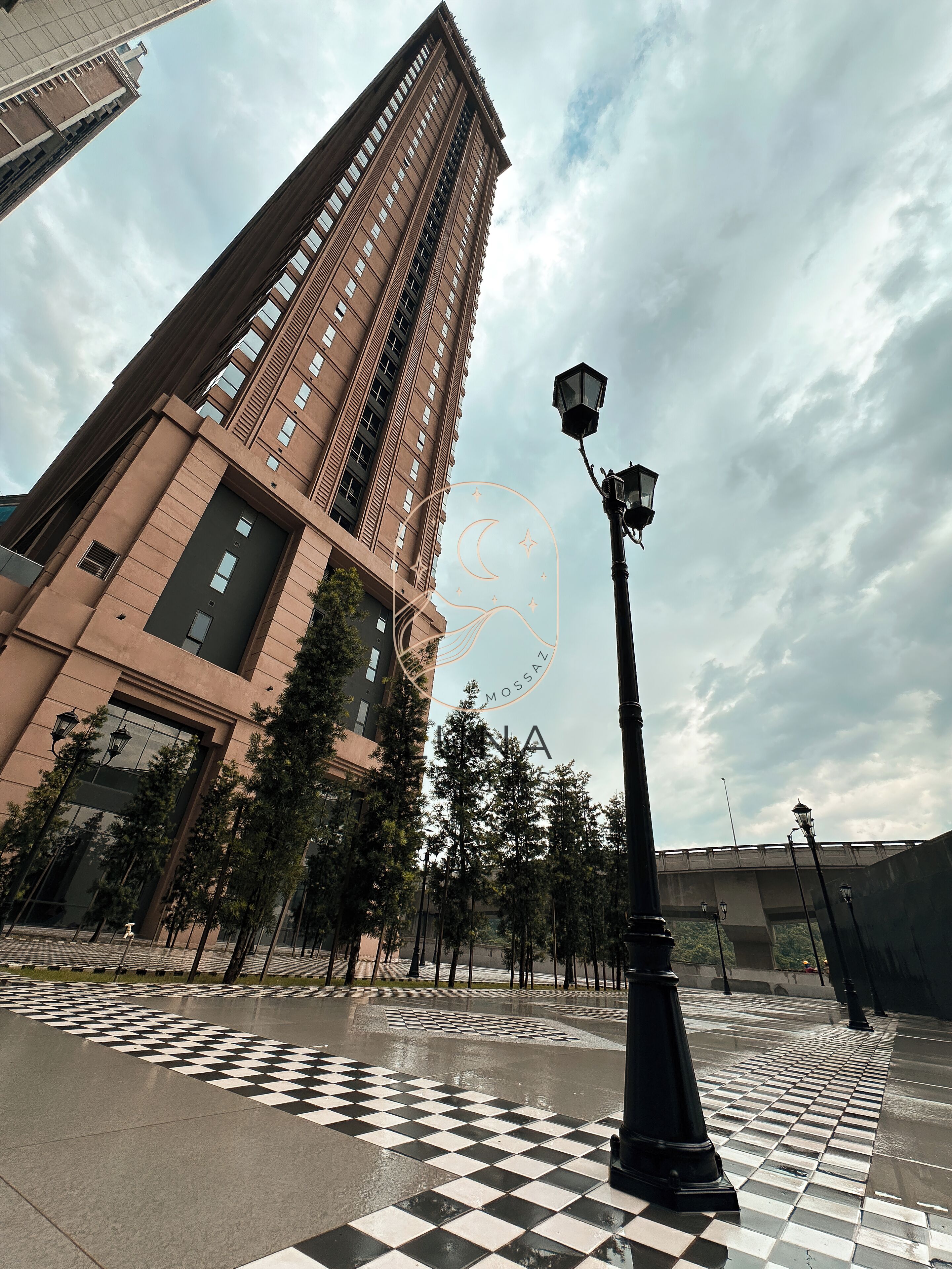 Un edificio alto con un diseño arquitectónico moderno, pavimento a cuadros y una farola.