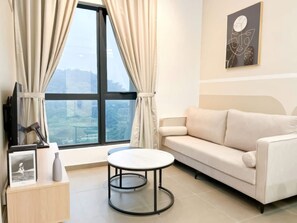 A modern living room with a sofa, a round table, a TV, and a window with curtains. - Ciao Mossaz Suites Luxury Apartments (Petaling Jaya)
