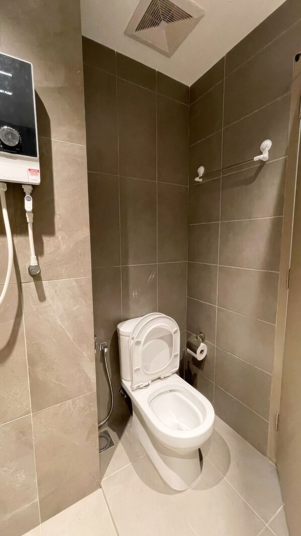 Une petite salle de bain moderne, équipée de toilettes, d’un sèche-mains et d’un porte-rouleau de papier toilette fixé au mur.