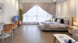 Une chambre d’hôtel moderne dotée d’un grand lit, d’un bureau, d’une chaise, d’un ventilateur de plafond et d’une grande fenêtre avec des rideaux légers.
