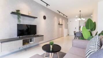 A modern living room with a flat-screen TV, a round coffee table, and a grey sofa.