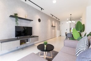 Una sala de estar moderna con un televisor de pantalla plana, una mesa de centro redonda y un sofá gris.