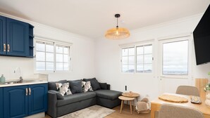 Eine moderne Küche mit blauen Schränken, einem grauen Sofa und einem Essbereich mit Tisch und Stühlen.