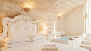 A bedroom with a large bed, a stone wall, a wooden headboard, a nightstand, a lamp, and a hot tub. - Reale - Suite with Jacuzzi in the Heart of Monopoli (Monopoli)