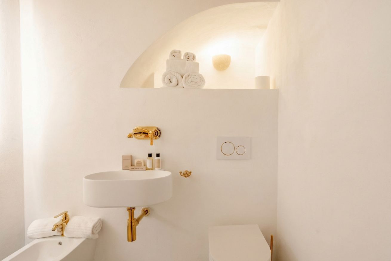 A bathroom with a white sink, gold fixtures, a toilet, and a towel rack with towels.