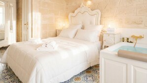 A bedroom with a large bed, a bathtub, and a stone wall. - Reale - Suite with Jacuzzi in the Heart of Monopoli (Monopoli)