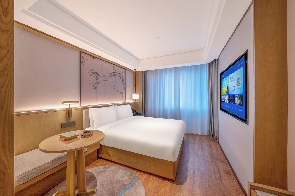 A hotel room with a bed, bedside table, lamp, and a TV mounted on the wall.