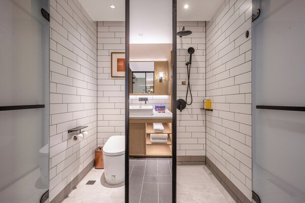 A modern bathroom with white subway tiles, a glass shower enclosure, a toilet, a sink with a mirror, and a towel rack. - Manxin Hotel (Wuhan)