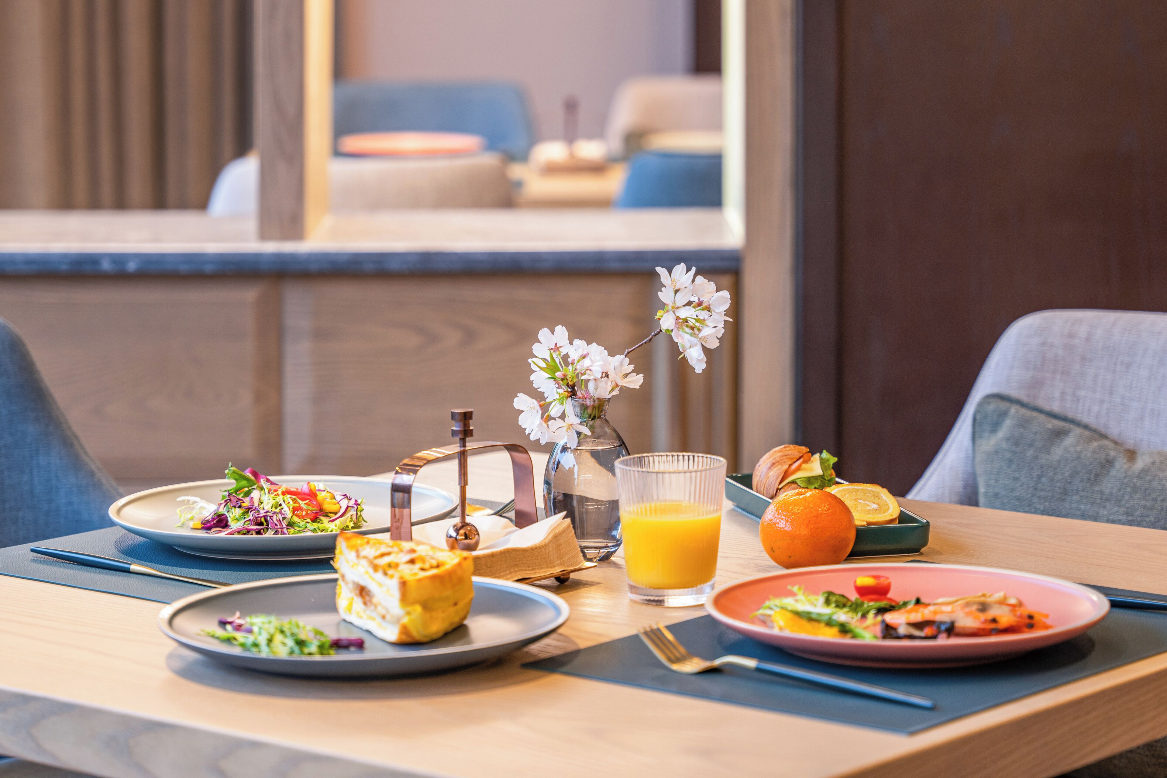 A breakfast table with plates of food, a glass of orange juice, and a vase with flowers.