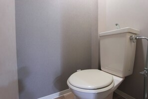 Une petite salle de bain propre, avec des toilettes blanches et un mur gris.