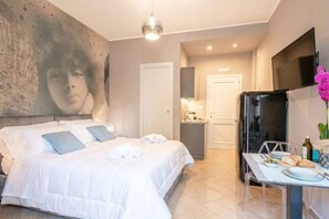 A hotel room with a bed, a dining table with plates and cutlery, a refrigerator, and a television mounted on the wall. - Coco - Elegance Boudoir (Bari)