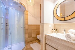 A modern bathroom with a glass-enclosed shower, a wooden vanity, and a round mirror. - Coco - Elegance Boudoir (Bari)